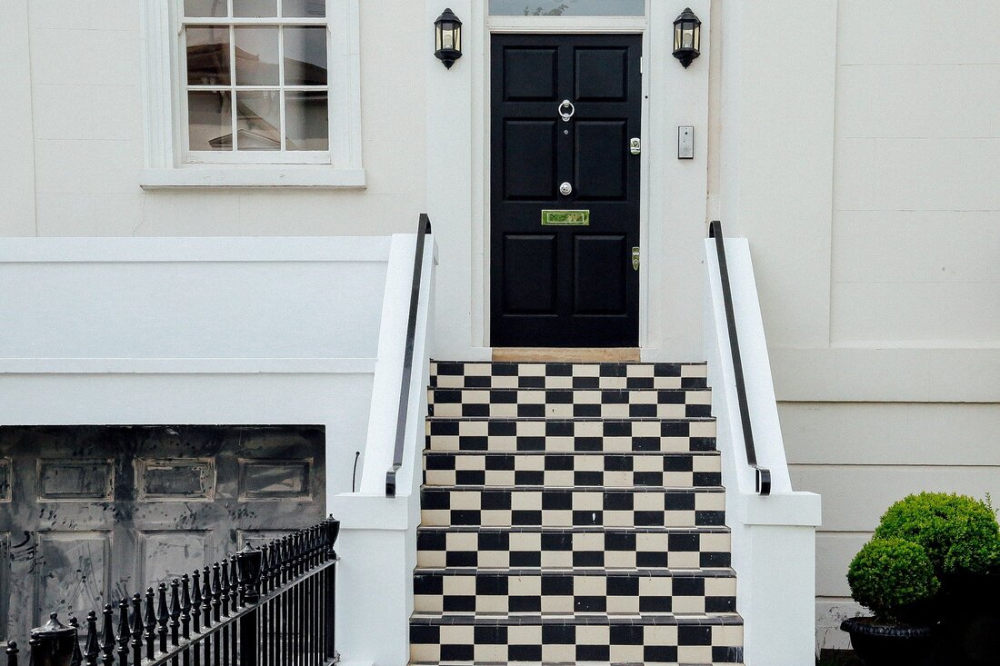 Picture of a georgian style town house with black and white chequered stair risers leading to a black timber front door. The house is finished in white painted render. 