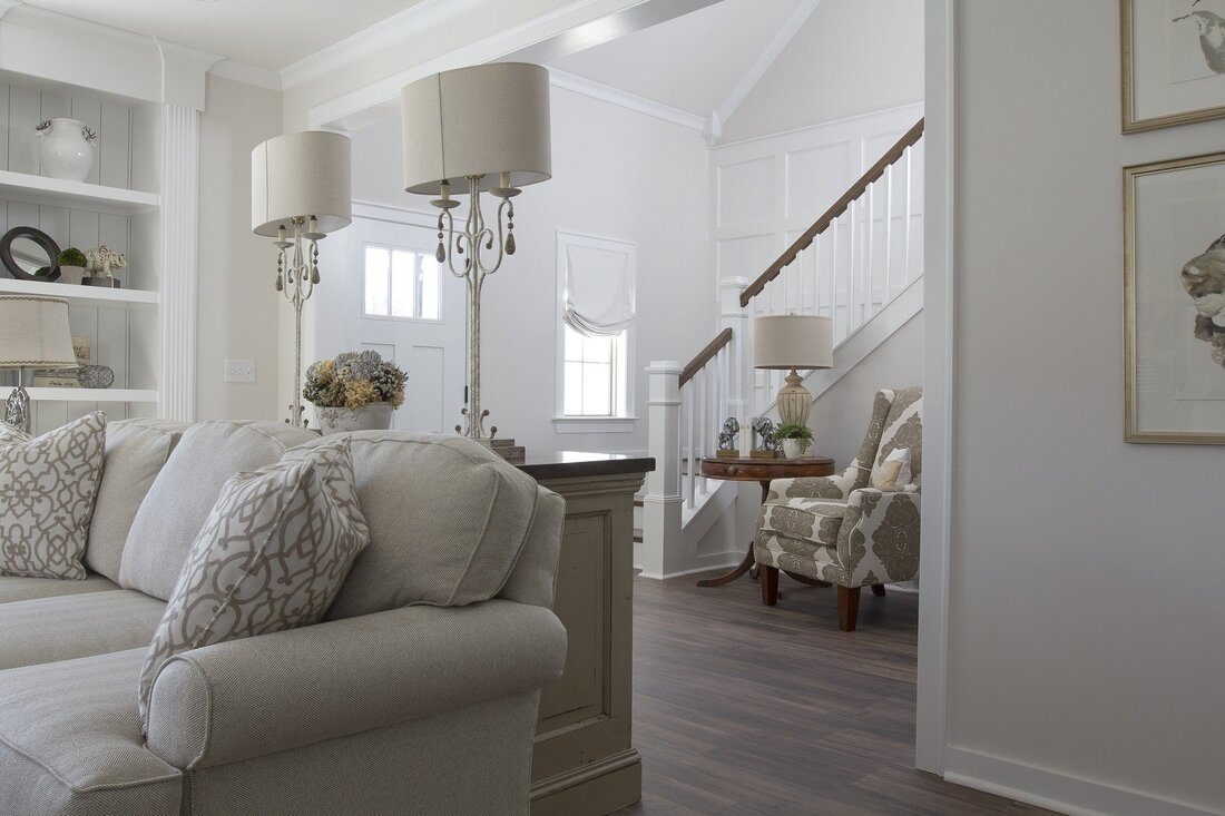 Picture of a traditional looking living room leading to the hall and satirs. The room is painted white and furnished in white, with dark oak flooring.