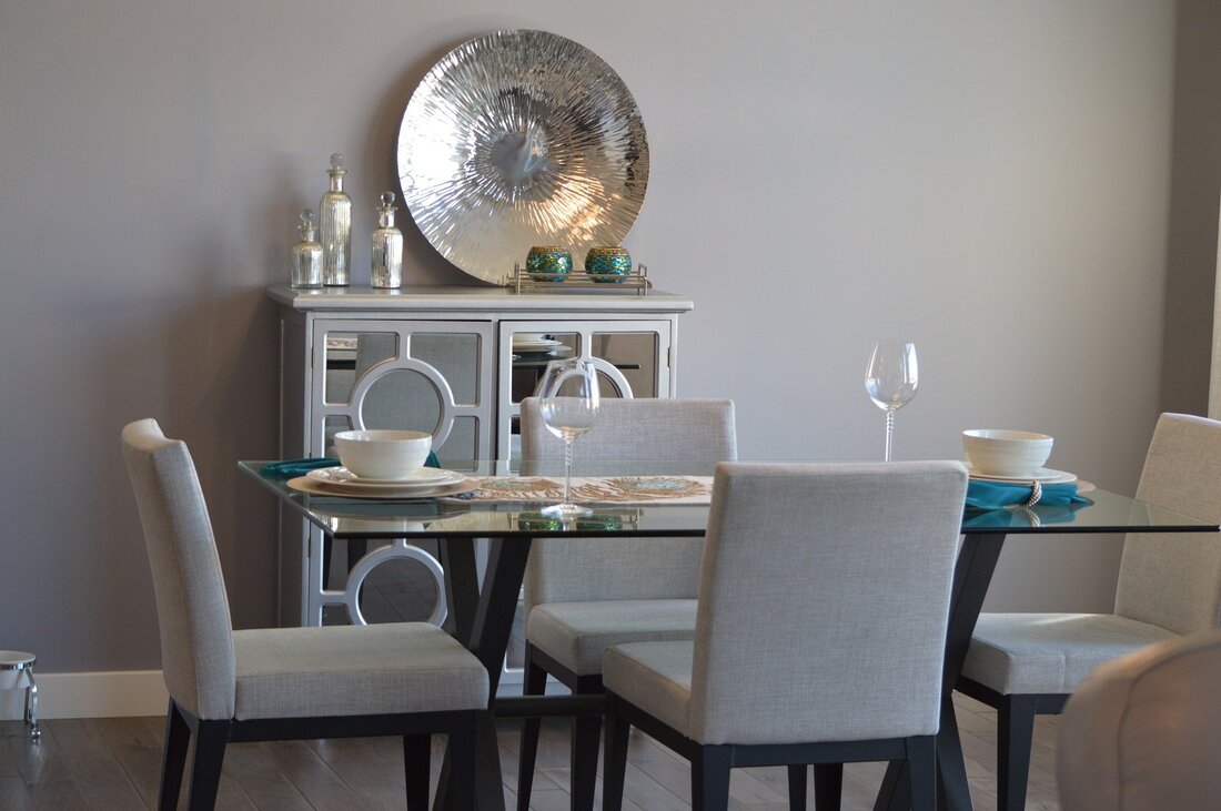 Picture of a dining table that is set for use. There is a cupboard behind the dining table that is dressed with showpieces in front of an arctic grey wall