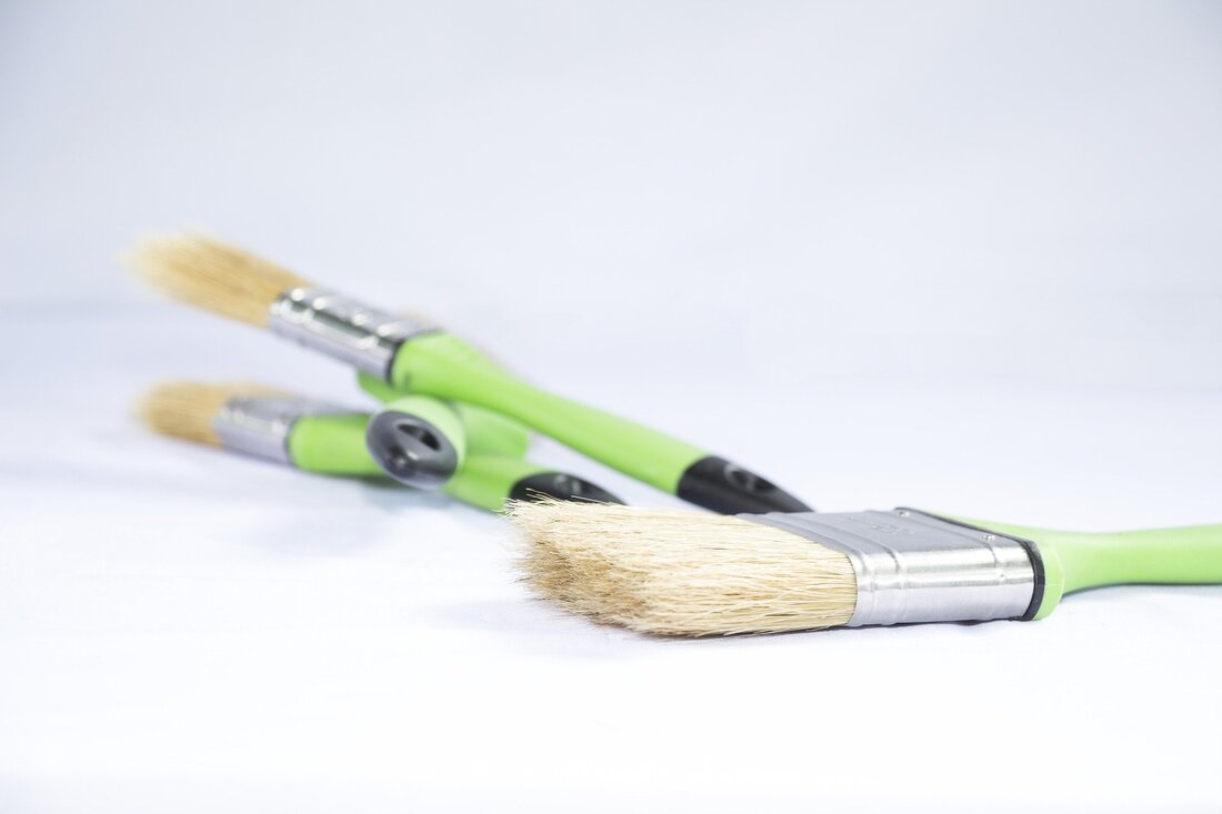 Picture of three paint brushes with lime green handles lying against a white background