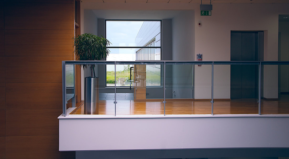 Picture of a modern office with a mezzanine floor. There is a lift lobby and glass screen to protect against falling between the floors. 