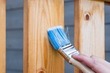 Picture of a blue paint brush painting making a brush stroke on a timber fence panel